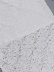 Flat fabric detail of a white lace maxi dress showing the floral lace pattern
