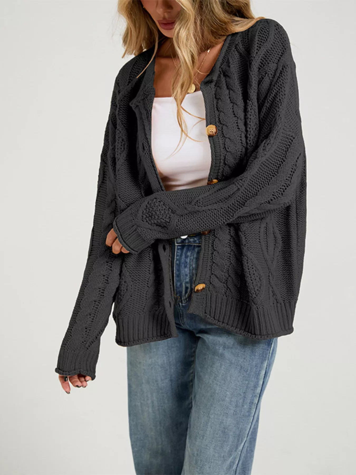 Side view of open dark gray cable knit cardigan over a white top with blue jeans