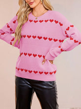 On-model front view of a pink dropped shoulder sweater with rows of red hearts