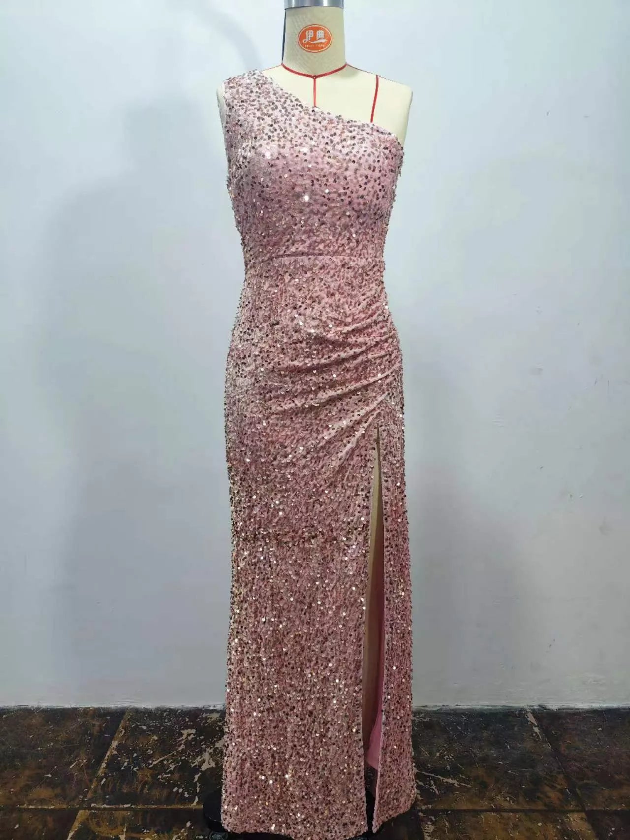 Pink sequin one shoulder evening dress shown front facing on a dress form with a high slit