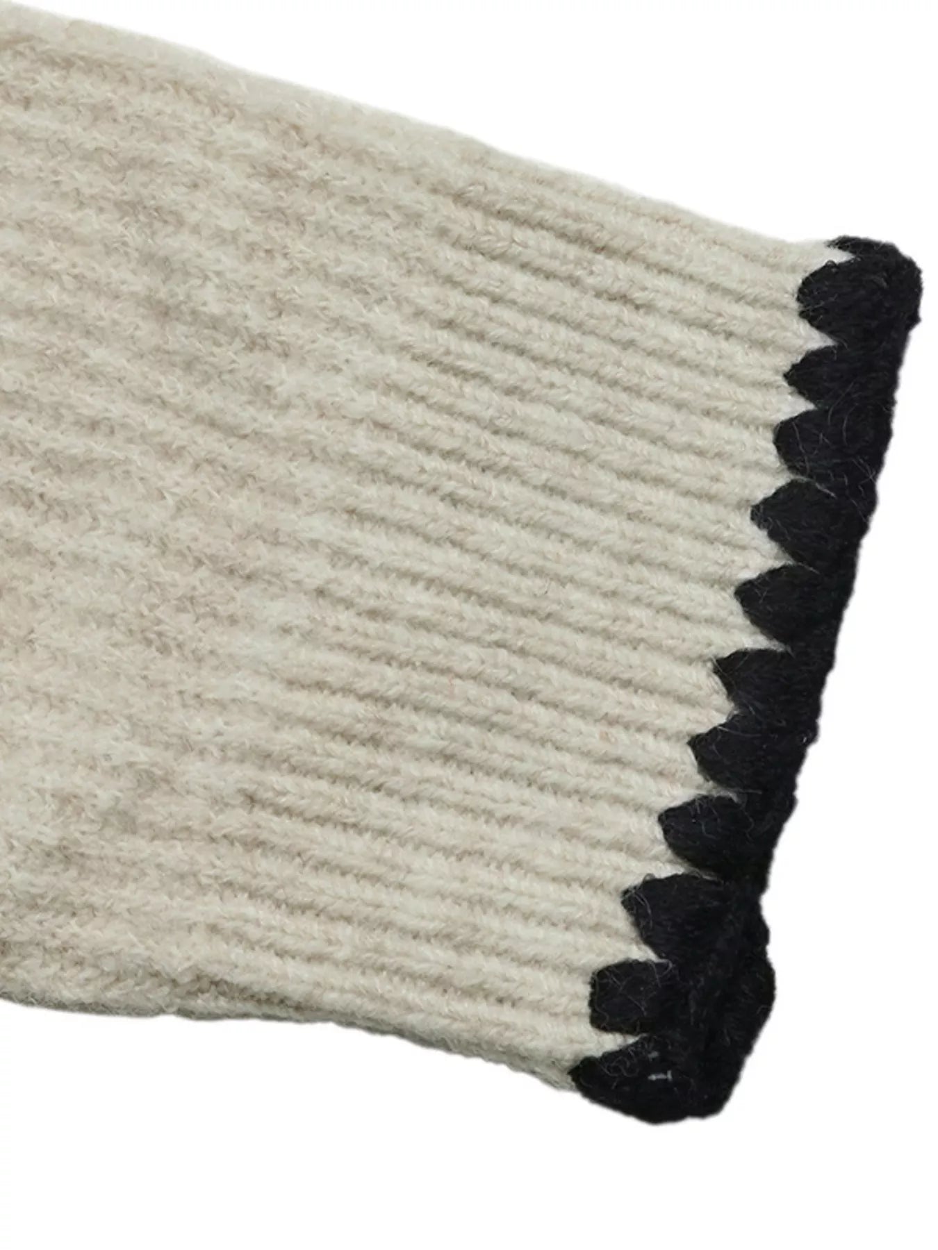 Close up of a cream ribbed cuff with black scalloped edge trim