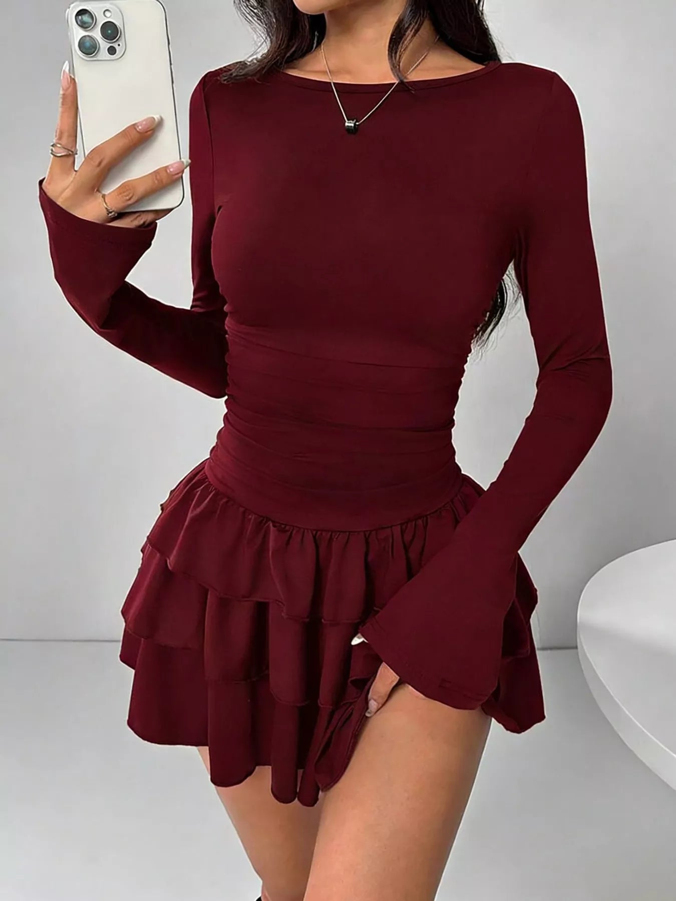 Burgundy layered ruffle long sleeve mini dress worn front facing in a mirror selfie holding a phone
