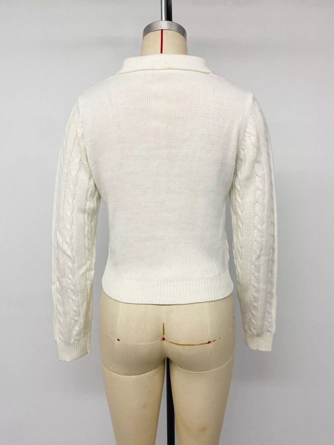 Back view of white cable knit long sleeve sweater on mannequin with ribbed hem