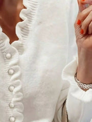 Close side view of a white ruffled sweater with pearl buttons
