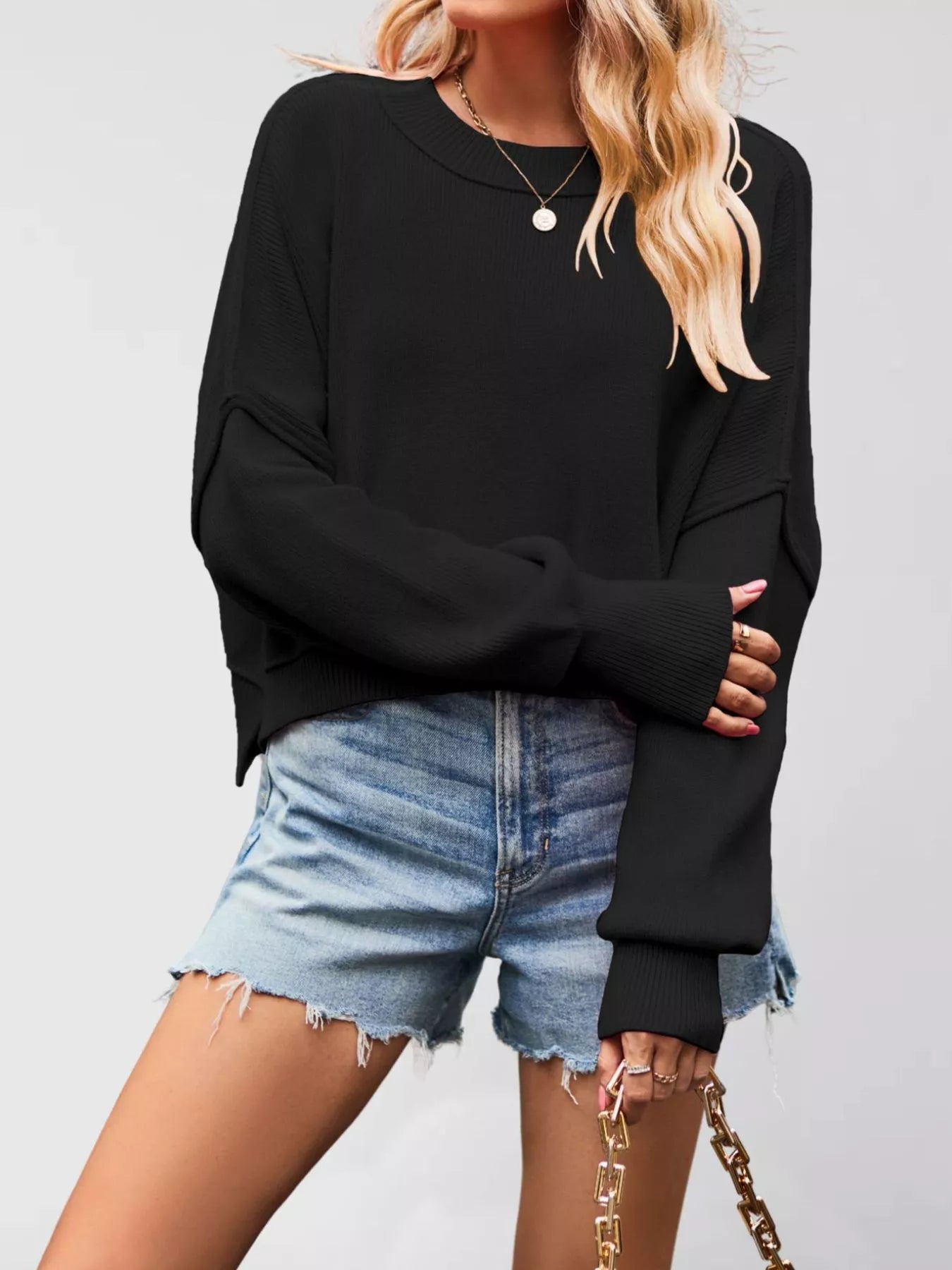 Front view of a black crew neck dropped shoulder sweater with ribbed cuffs worn with denim shorts.