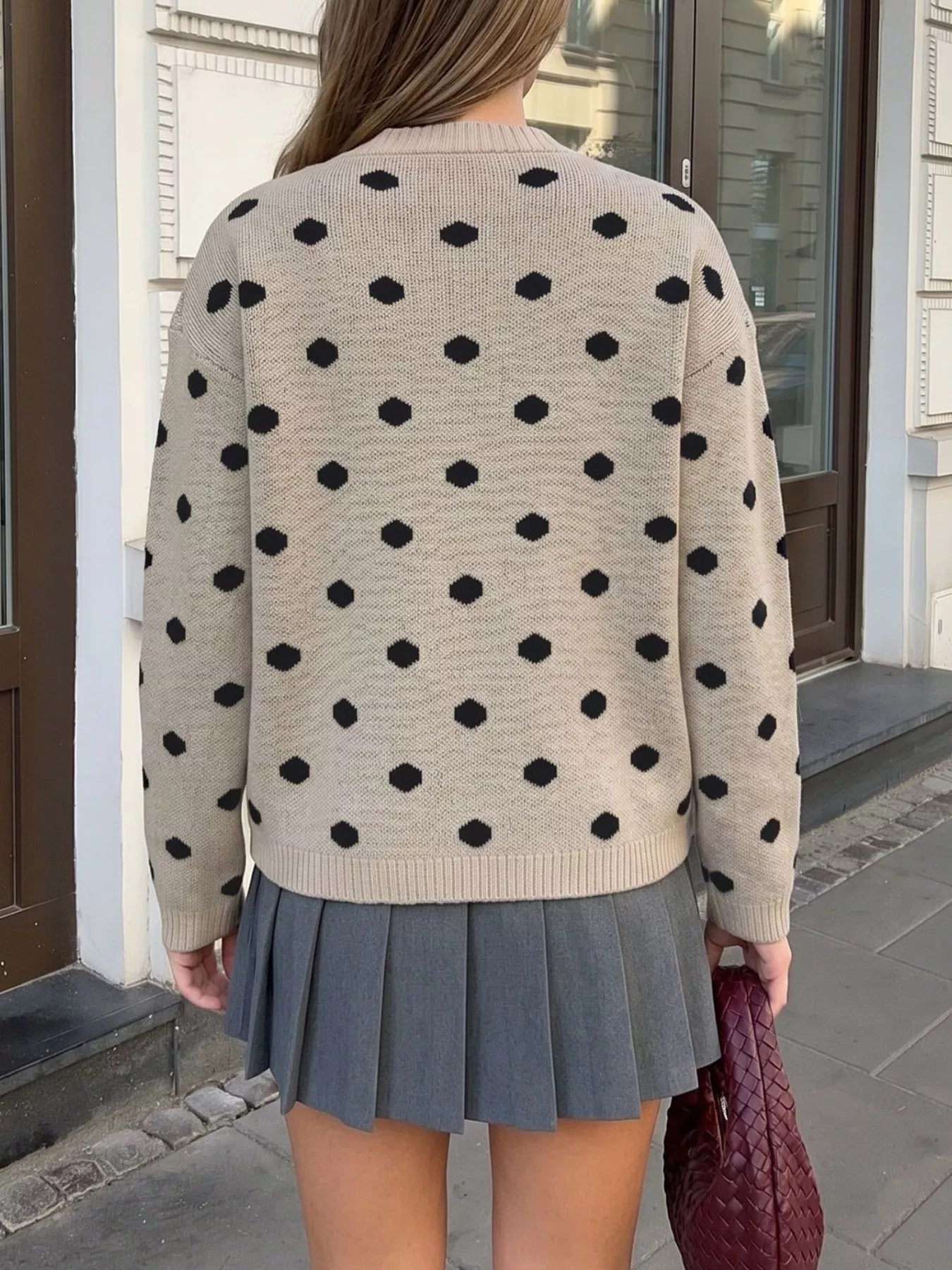 Back view of khaki polka dot dropped shoulder sweater with grey pleated skirt