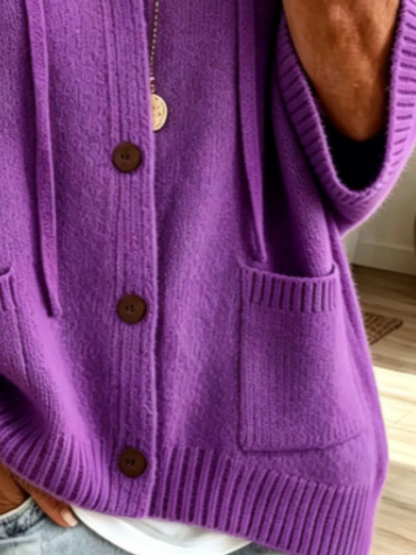 Detail view of the purple cardigan showing brown buttons, patch pockets and ribbed hem