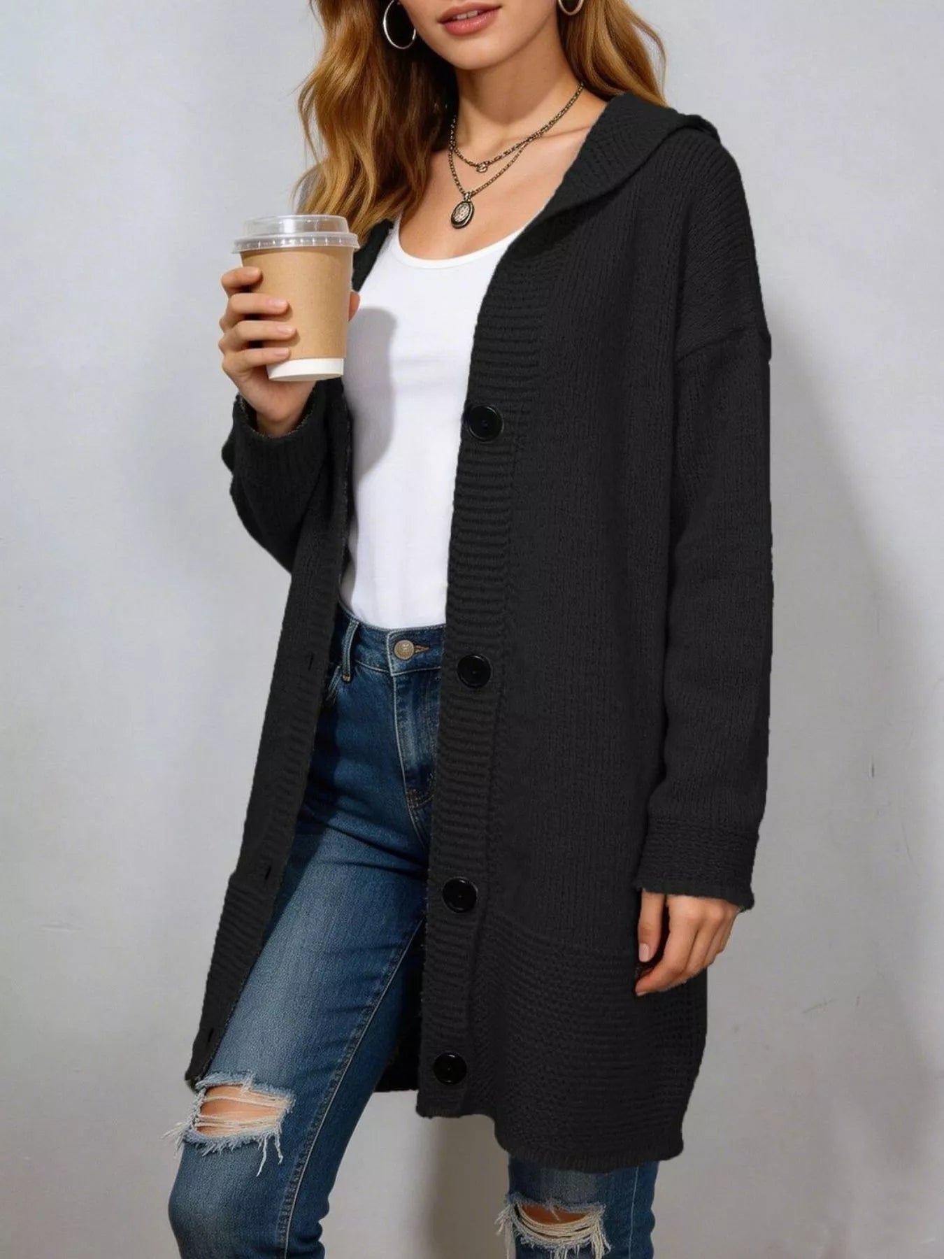 Long black hooded knit cardigan with black buttons worn open over jeans