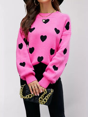 Front view of the hot pink dropped shoulder sweater with black hearts, holding a black handbag.
