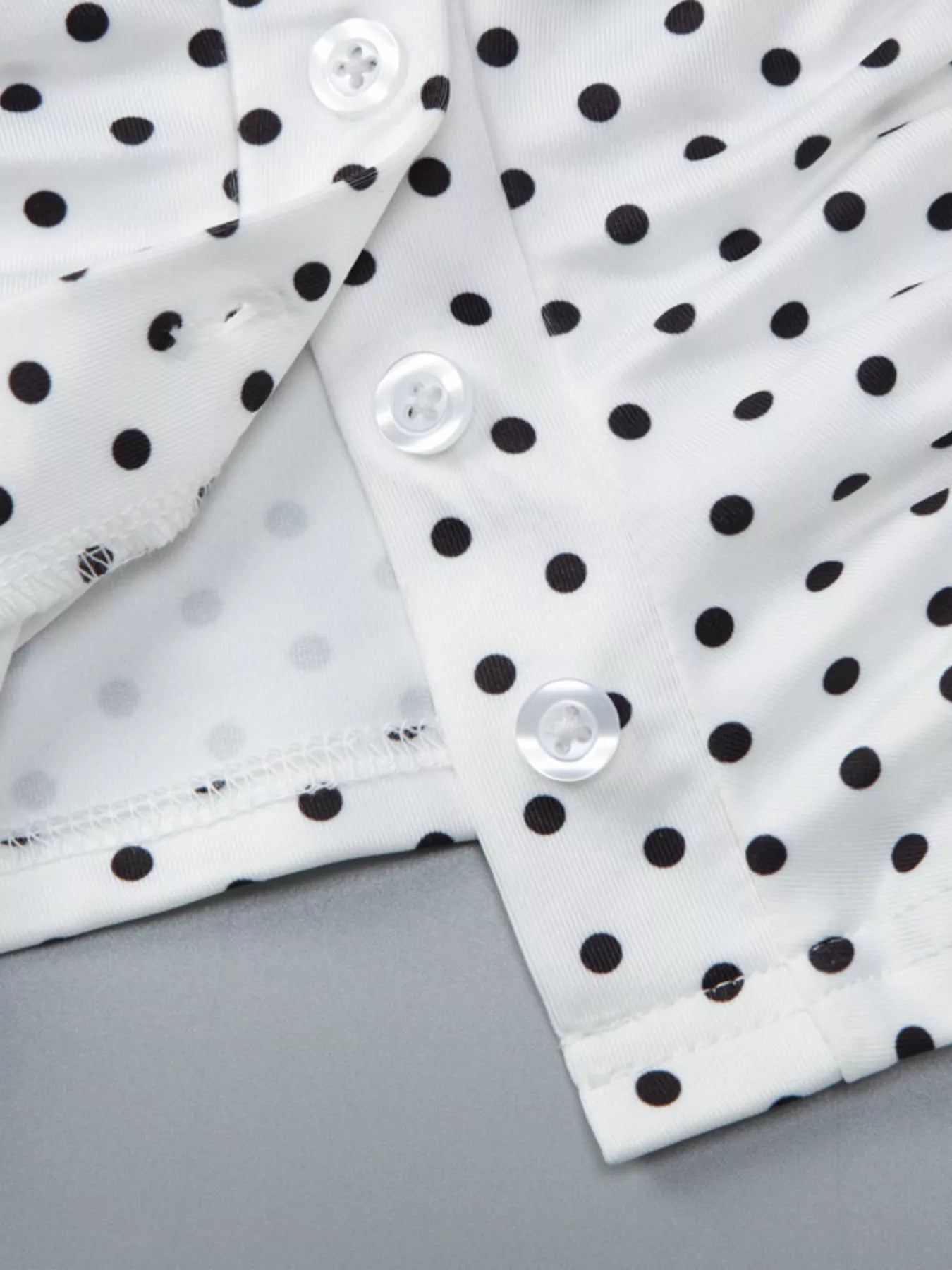 Close-up detail of white polka dot top showing V-neck, ruched fabric, buttons, and cuff.