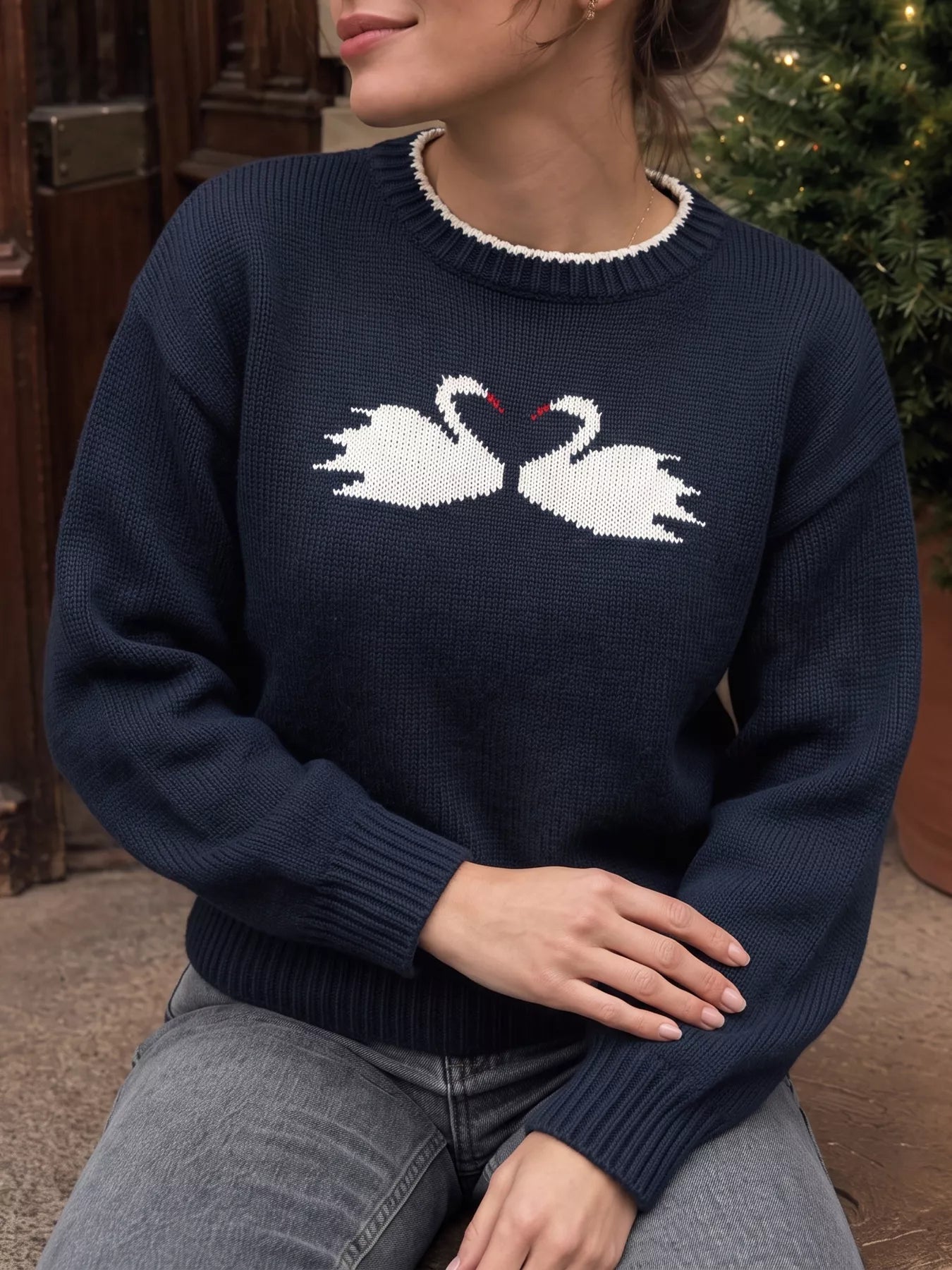 Seated front view of a navy dropped shoulder sweater with white swan pair motif