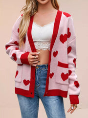 Pink knit cardigan with red hearts worn open over a white lace top