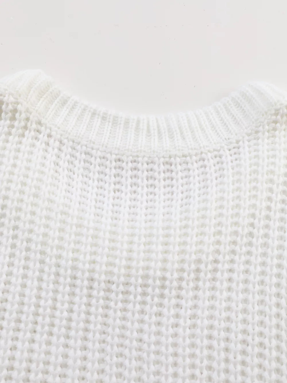 Close view of the back neckline of a white ribbed knit sweater showing knit texture.