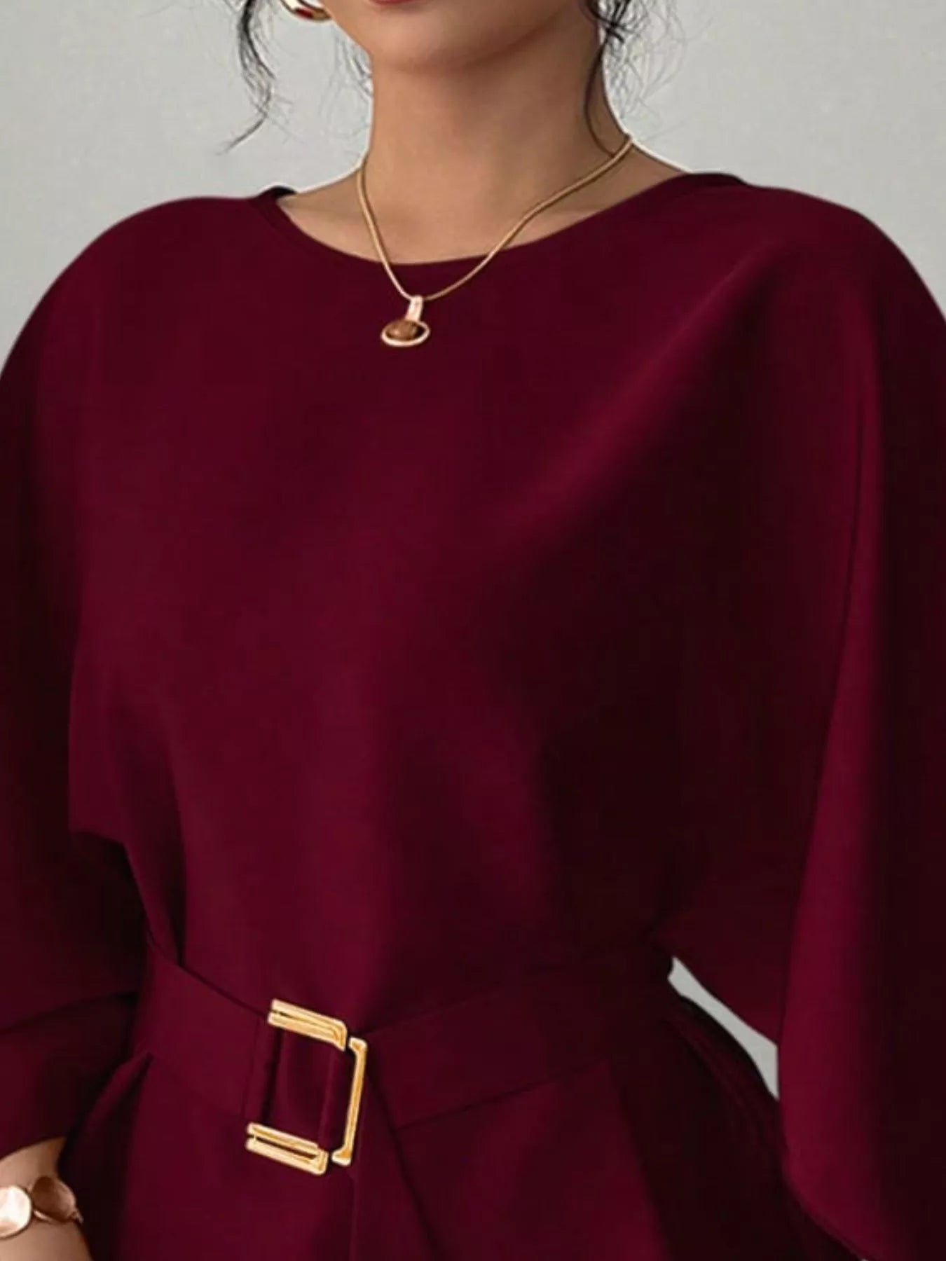 Close view of burgundy round neck blouse showing neckline and gold buckle belt
