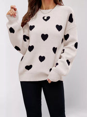 Front view of a cream dropped shoulder sweater with black hearts, one arm raised.