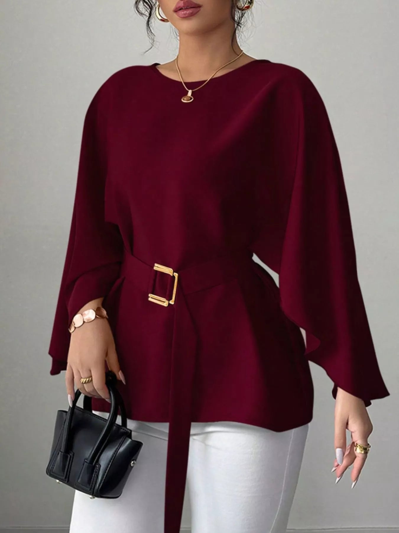 Burgundy round neck blouse front view holding black handbag with gold buckle belt