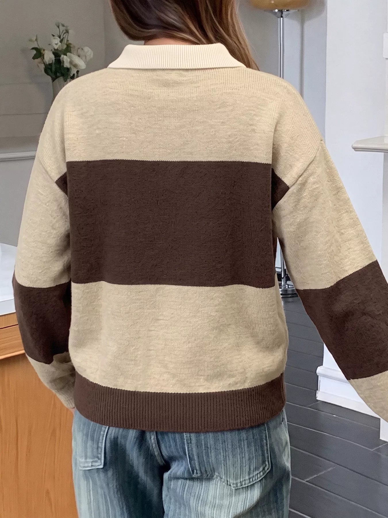 Back view of beige and brown color block polo sweater with brown ribbed hem.