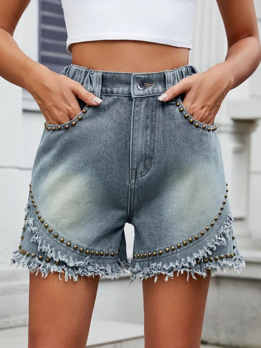 Women's studded denim shorts with washed detailing, raw hems, and pockets.
