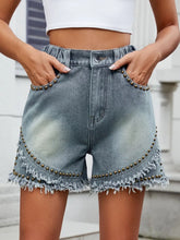 Women's studded denim shorts with washed detailing, raw hems, and pockets.