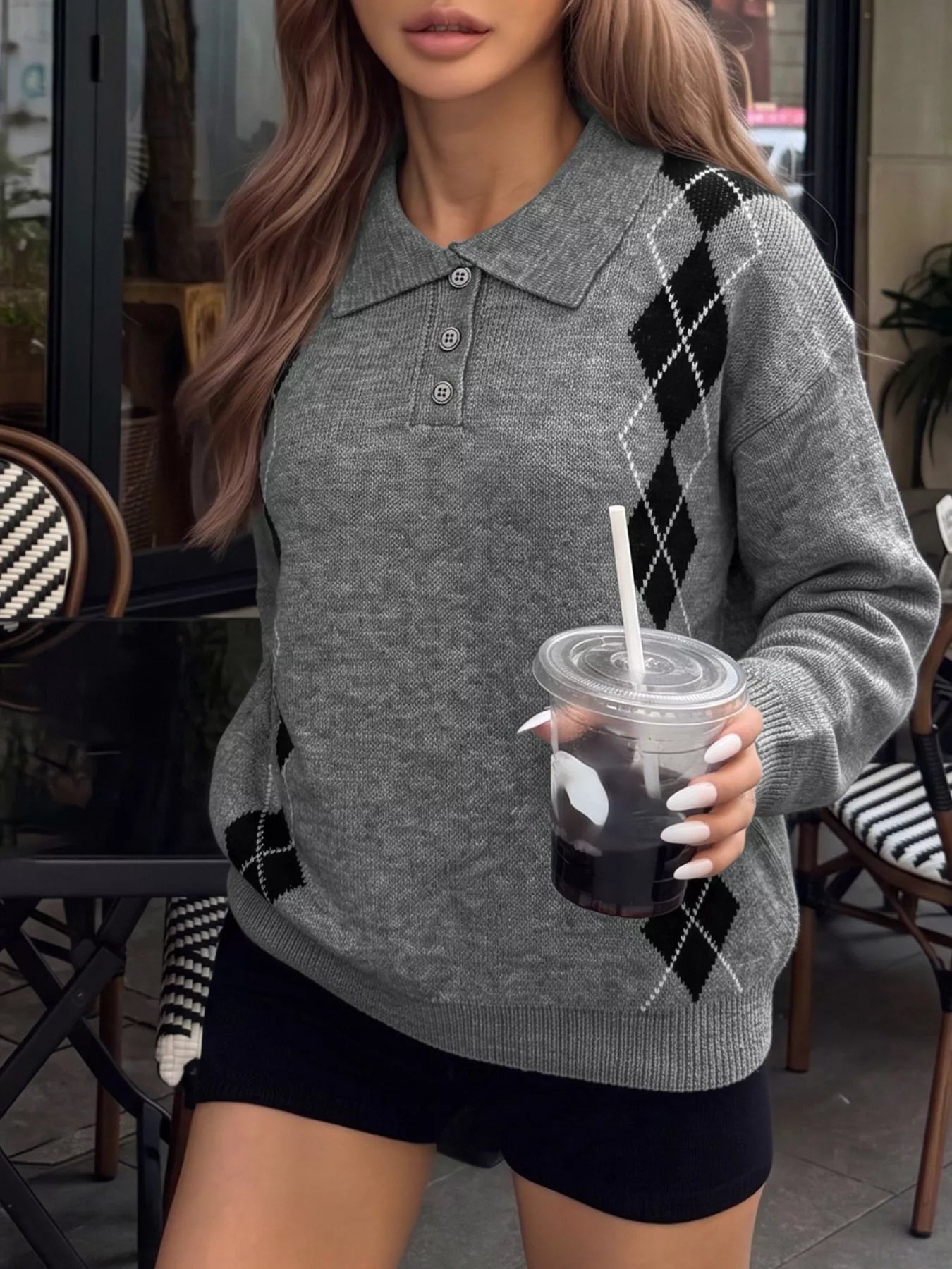 Front view of a gray argyle polo sweater with a three-button placket, holding a drink