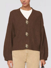 Brown V neck knit cardigan with large gold buttons worn over beige trousers