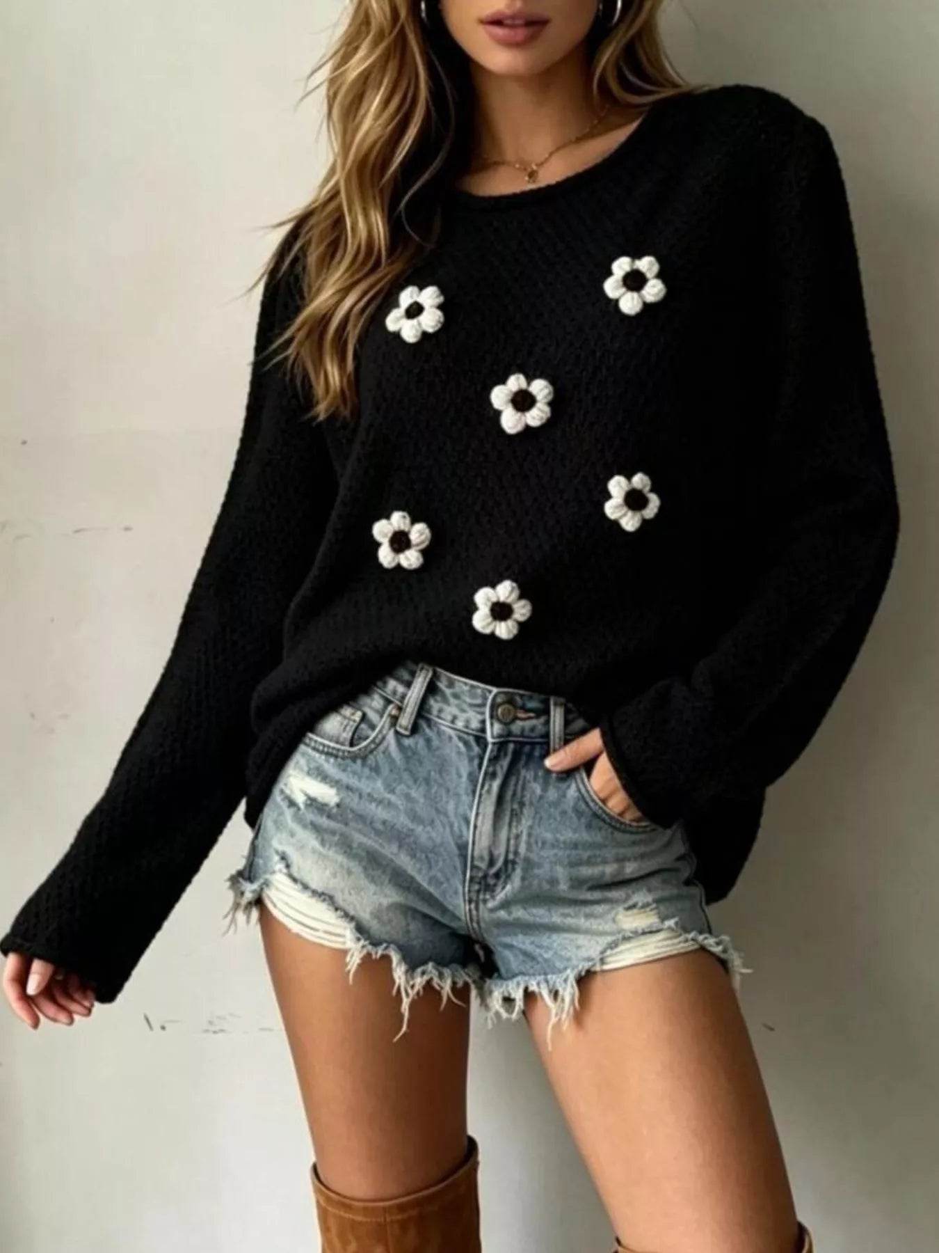 Front view of a black textured knit sweater with white floral appliques and long sleeves