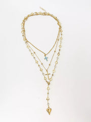 Layered gold necklaces laid flat on white background with blue cross and heart pendant