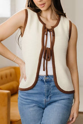 On-model front view of a beige tie front sweater vest with brown contrast trim