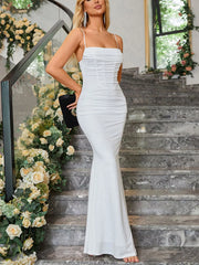 Side view of a white ruched spaghetti strap bodycon maxi dress holding a black clutch on stairs
