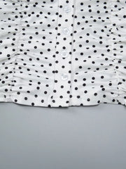 Close-up detail of white polka dot top showing ruched sides, V-neck seam, and front buttons