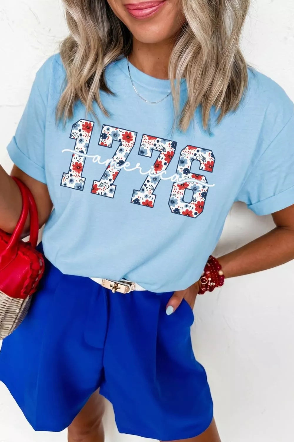 Women's light blue relaxed T-shirt featuring floral-print “1776” lettering and white America script detail.