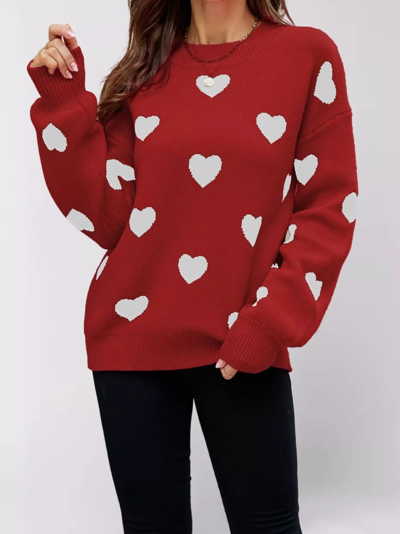 Front view of a red dropped shoulder sweater with white hearts, one arm raised.