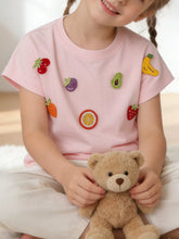 On-model front view of blush pink children's round neck t-shirt with scattered crochet fruit appliques