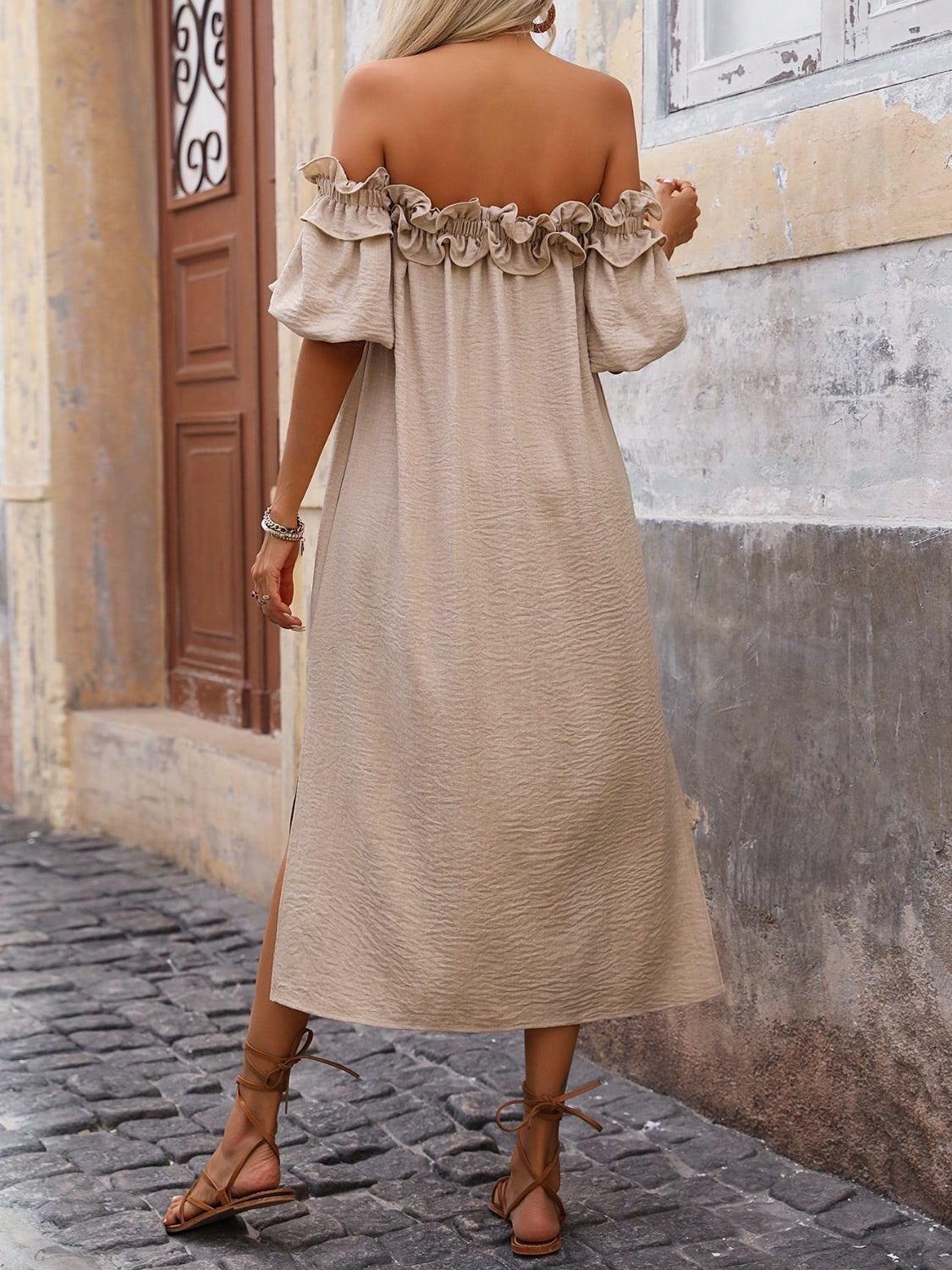 Back view of women's tan off-shoulder midi dress with ruffled trim and puff sleeves, styled on model.