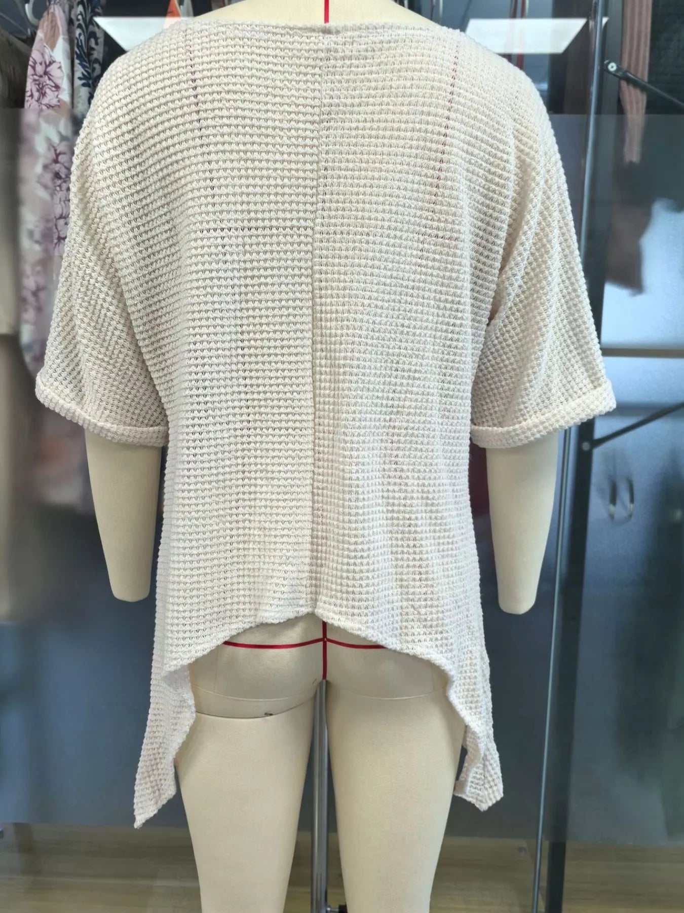 Back view of a white loose knit cover-up with an asymmetrical hem on a mannequin