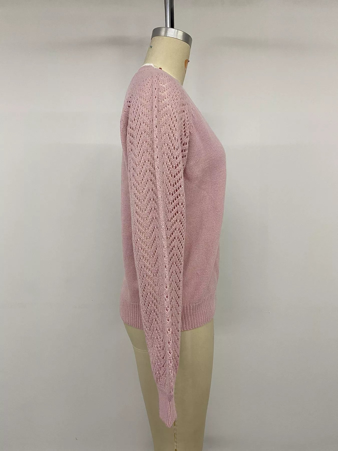 Side view on a mannequin of a pink V neck sweater with openwork long sleeves.