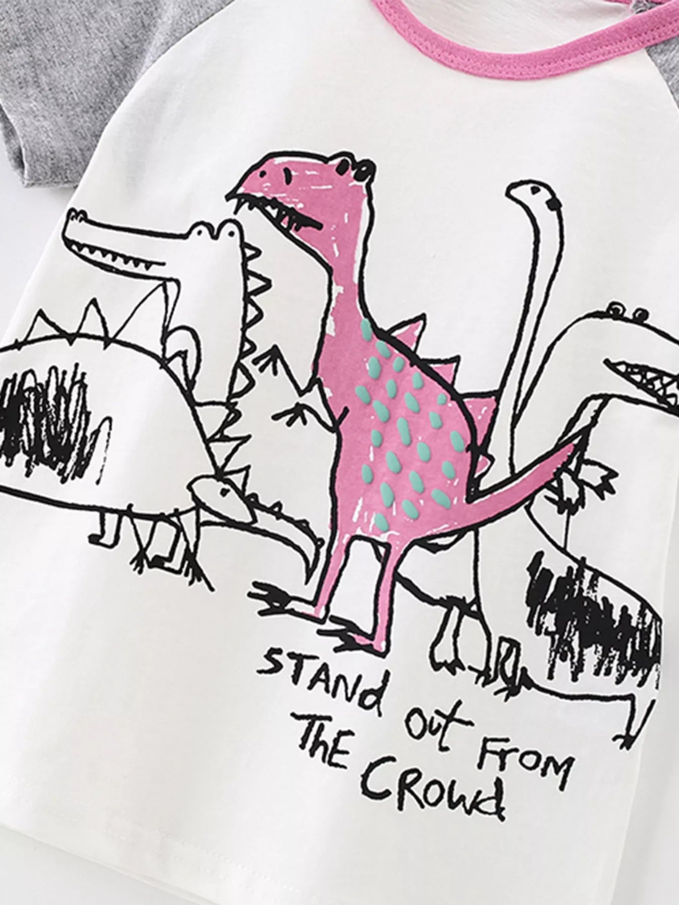 Close-up detail of the pink spotted dinosaur and sketched dinosaurs on white fabric