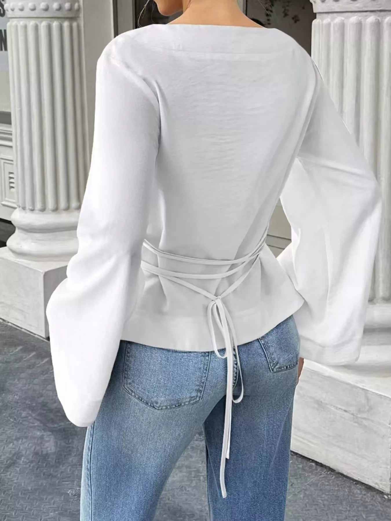 Back view of white boat neck long sleeve top with waist ties and flared sleeves on model