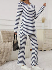Women's blue and white striped long sleeve top and flared pants set, standing with a black handbag, side slit visible.