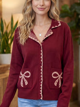 Burgundy knit cardigan with cream lace trim and bow pockets on model