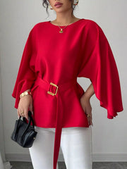 Red batwing sleeve blouse with gold buckle belt worn on model front view holding black handbag