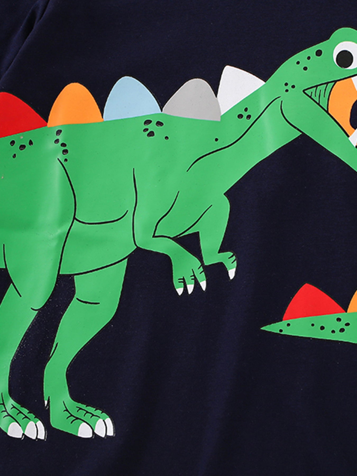 Close-up of the green dinosaur graphic with colorful back plates on a black children's short sleeve T-shirt