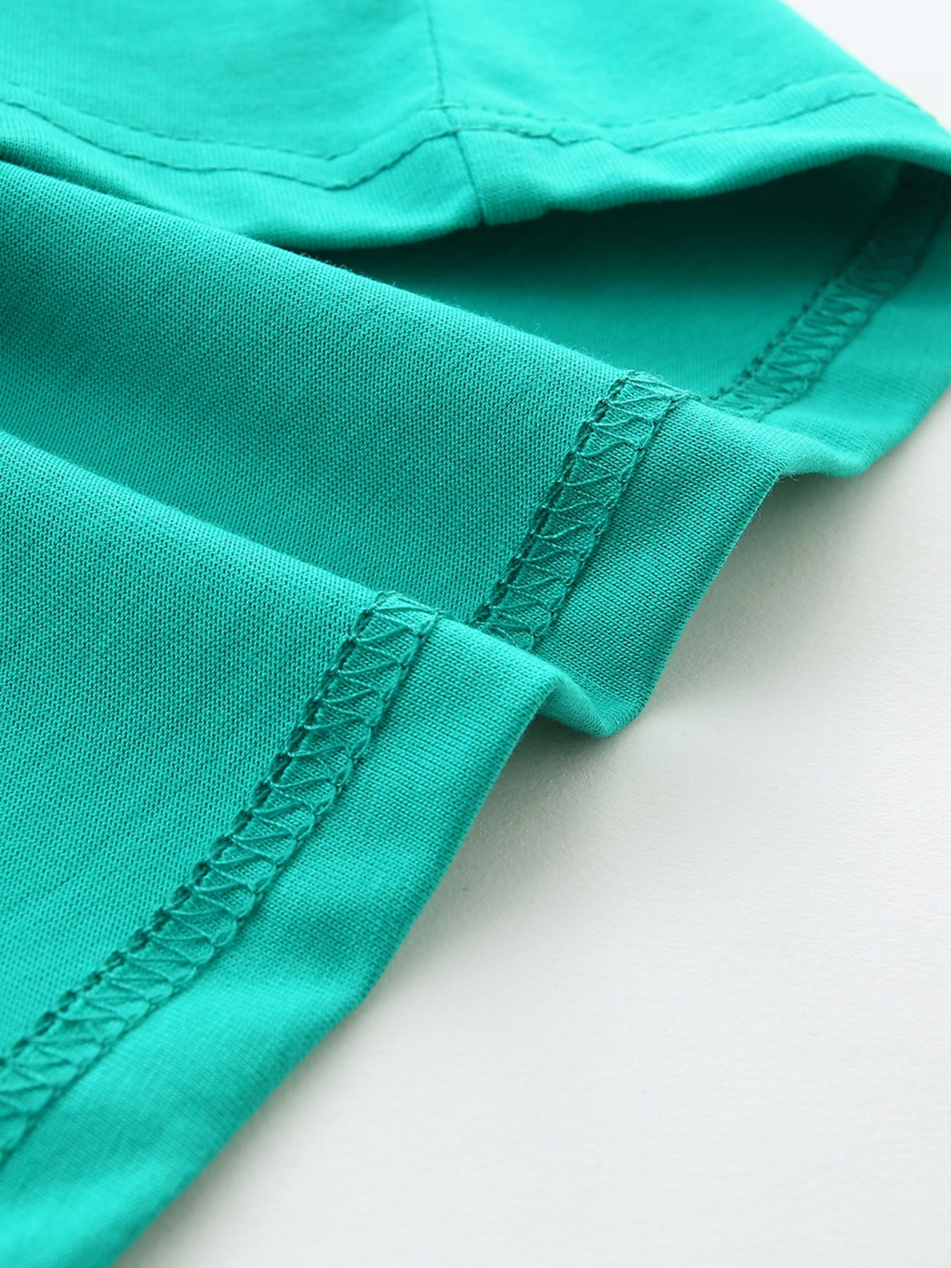 Close-up of turquoise t-shirt hem stitching showing the folded fabric and neat seams