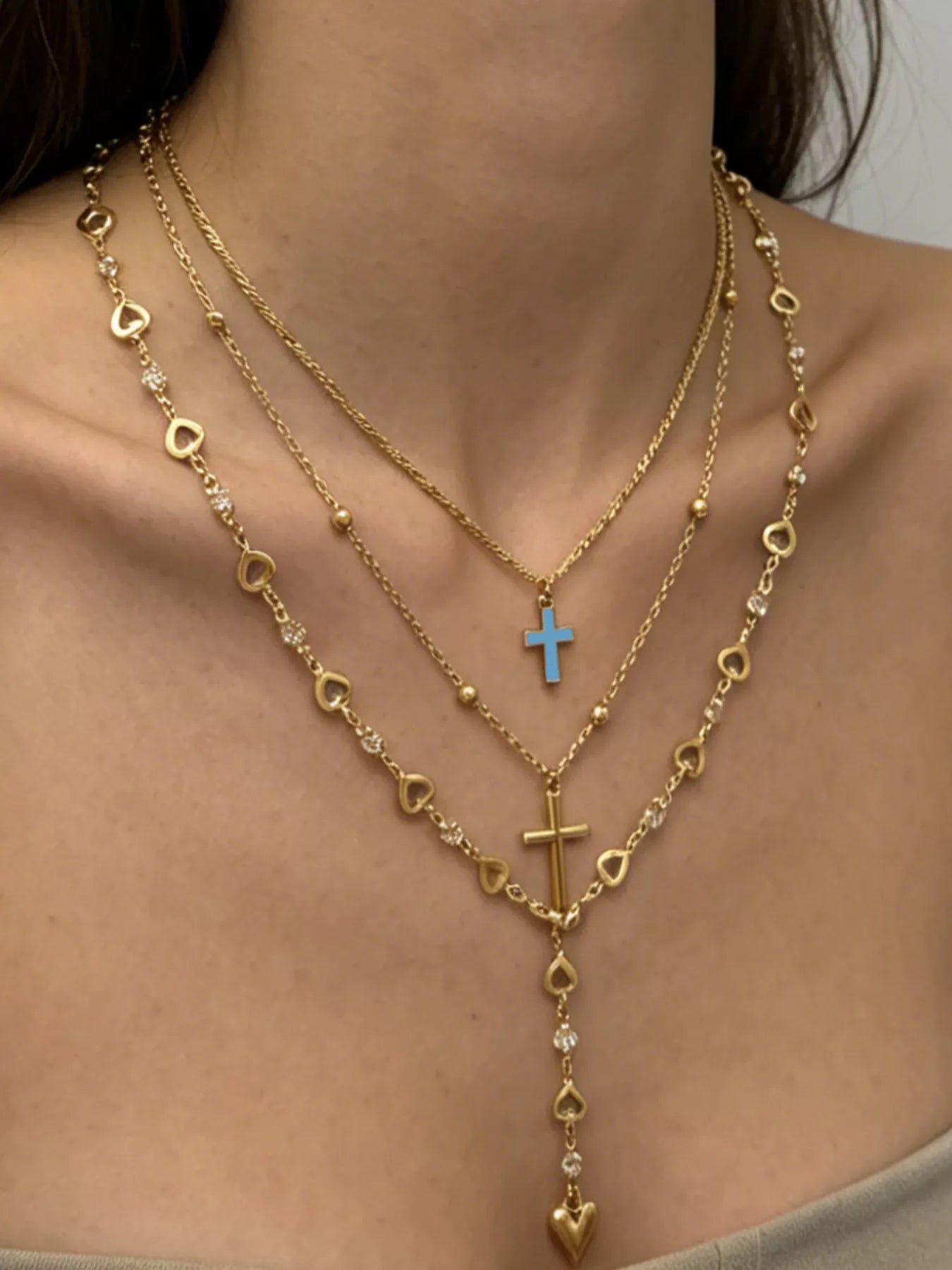 Layered gold necklaces on model showing blue cross, gold cross and dangling heart pendant
