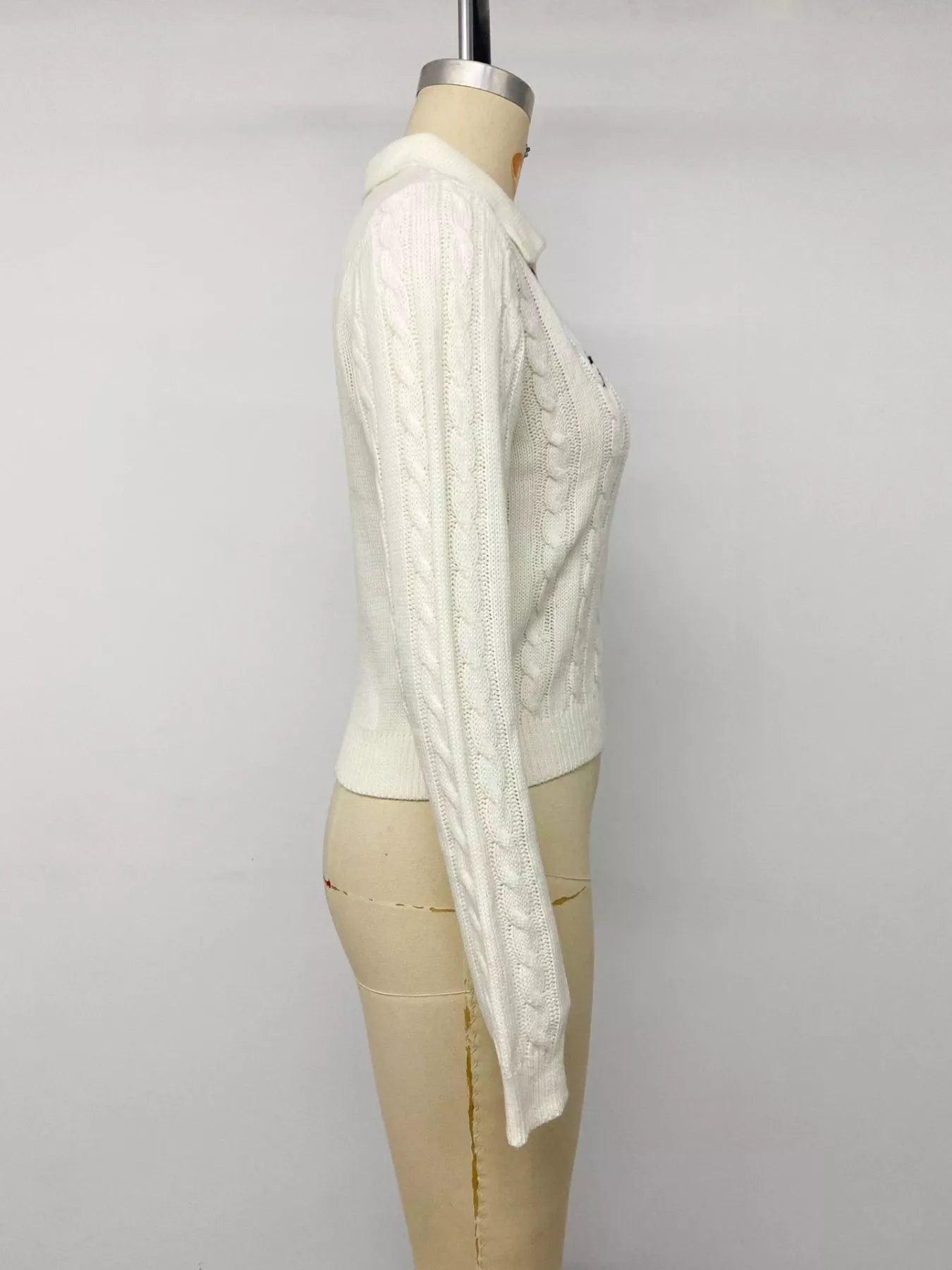 Side view of white cable knit long sleeve sweater on mannequin showing dropped shoulder