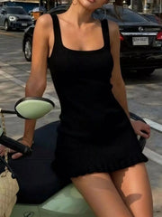 Front view of a black ribbed knit square neck dress, seated outdoors.
