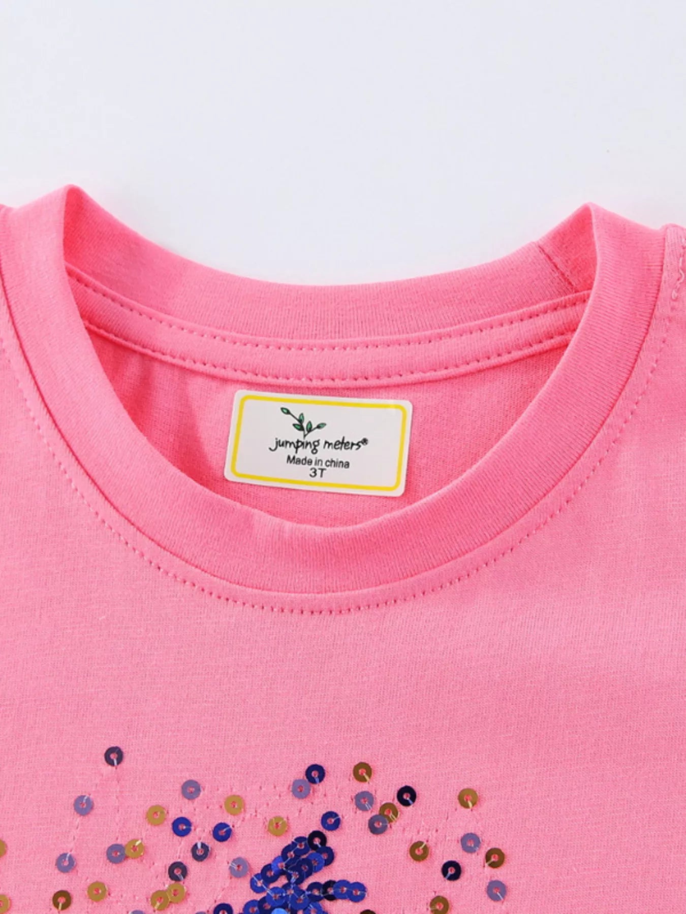 Close-up of fuchsia pink children's round neck tee neckline, stitching and sequin star below