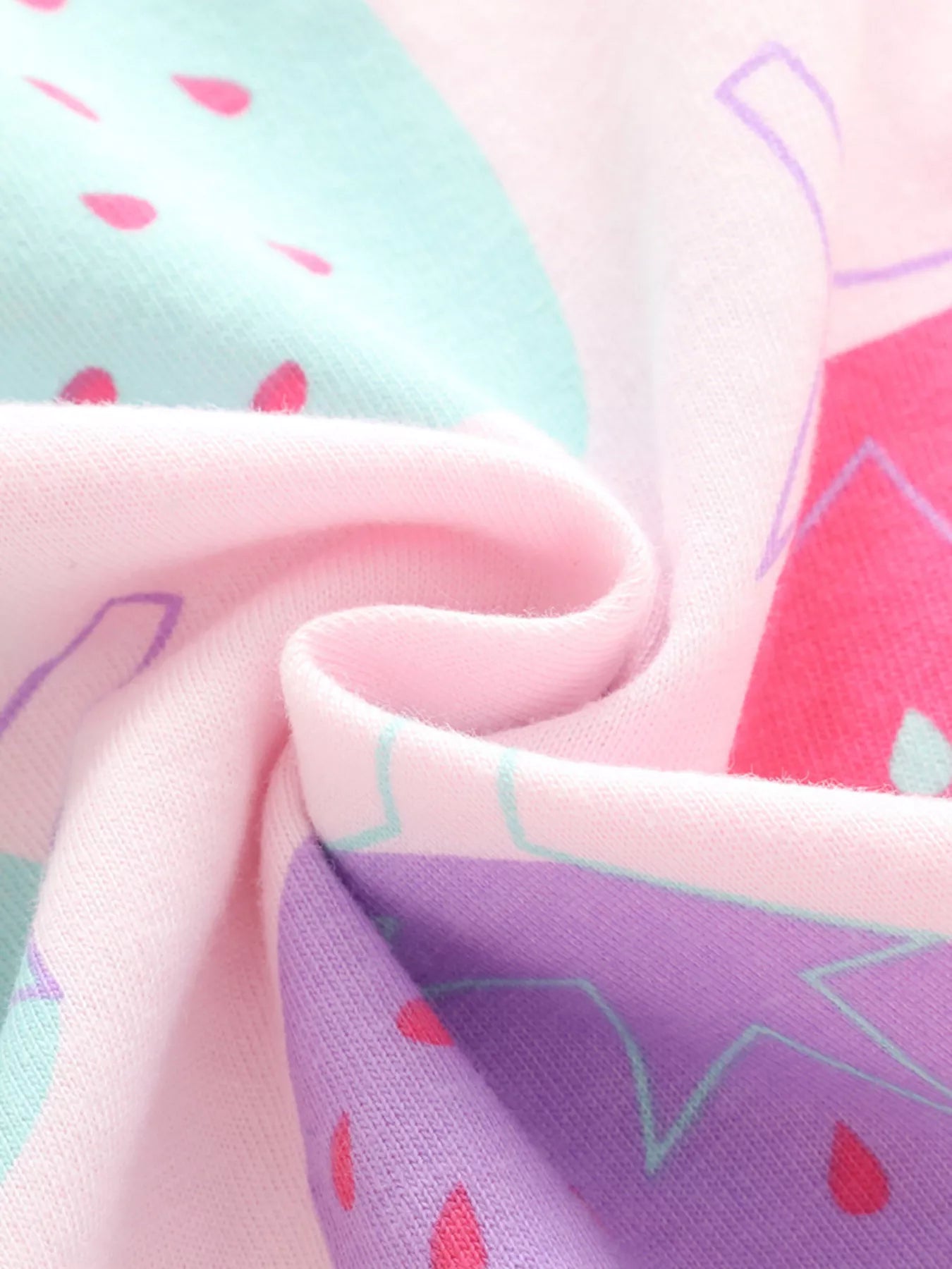 Close-up of soft pink fabric with colorful strawberry print, gathered in folds