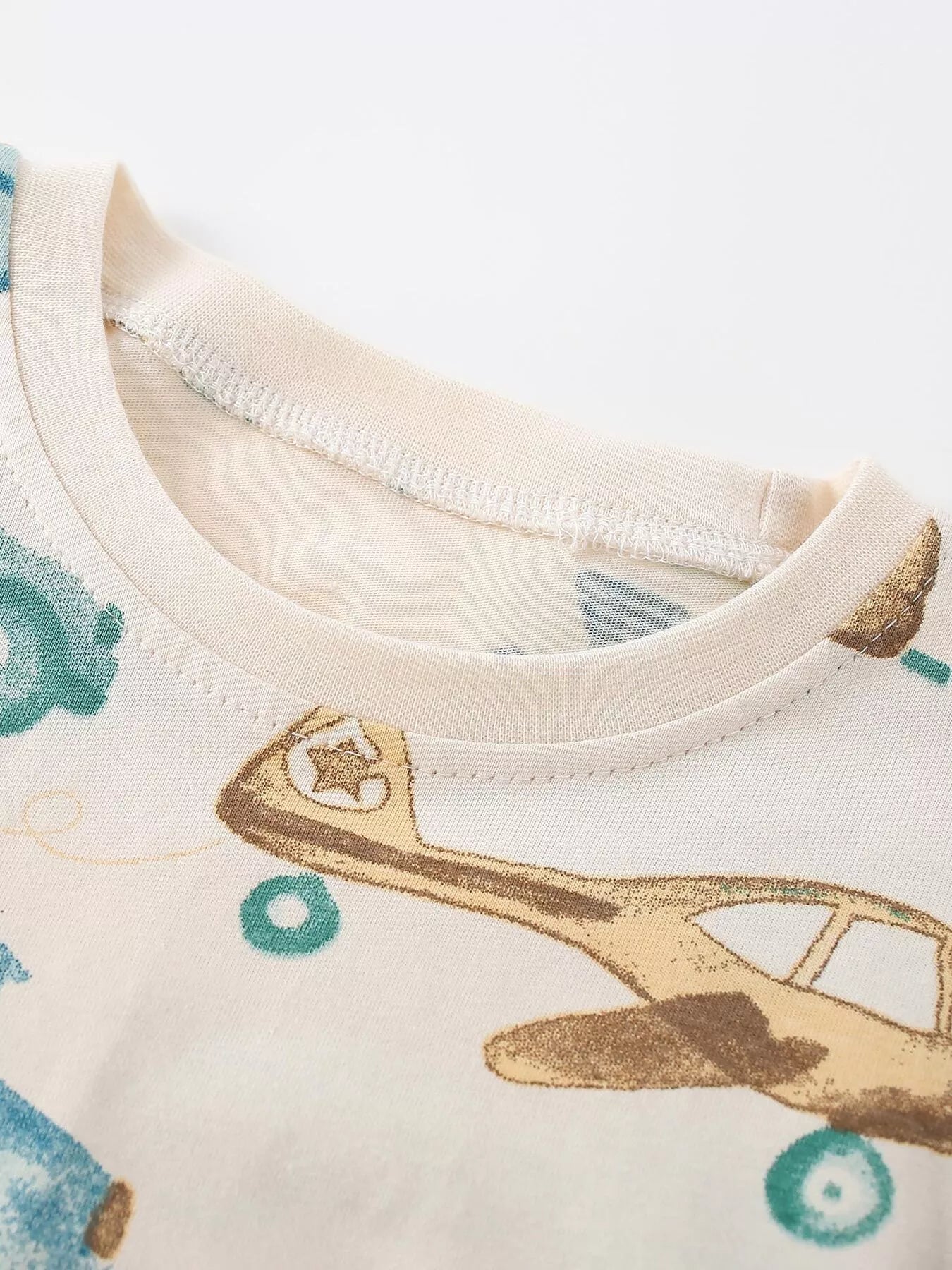 Close up of the cream crew neckline and a tan airplane from the transportation print