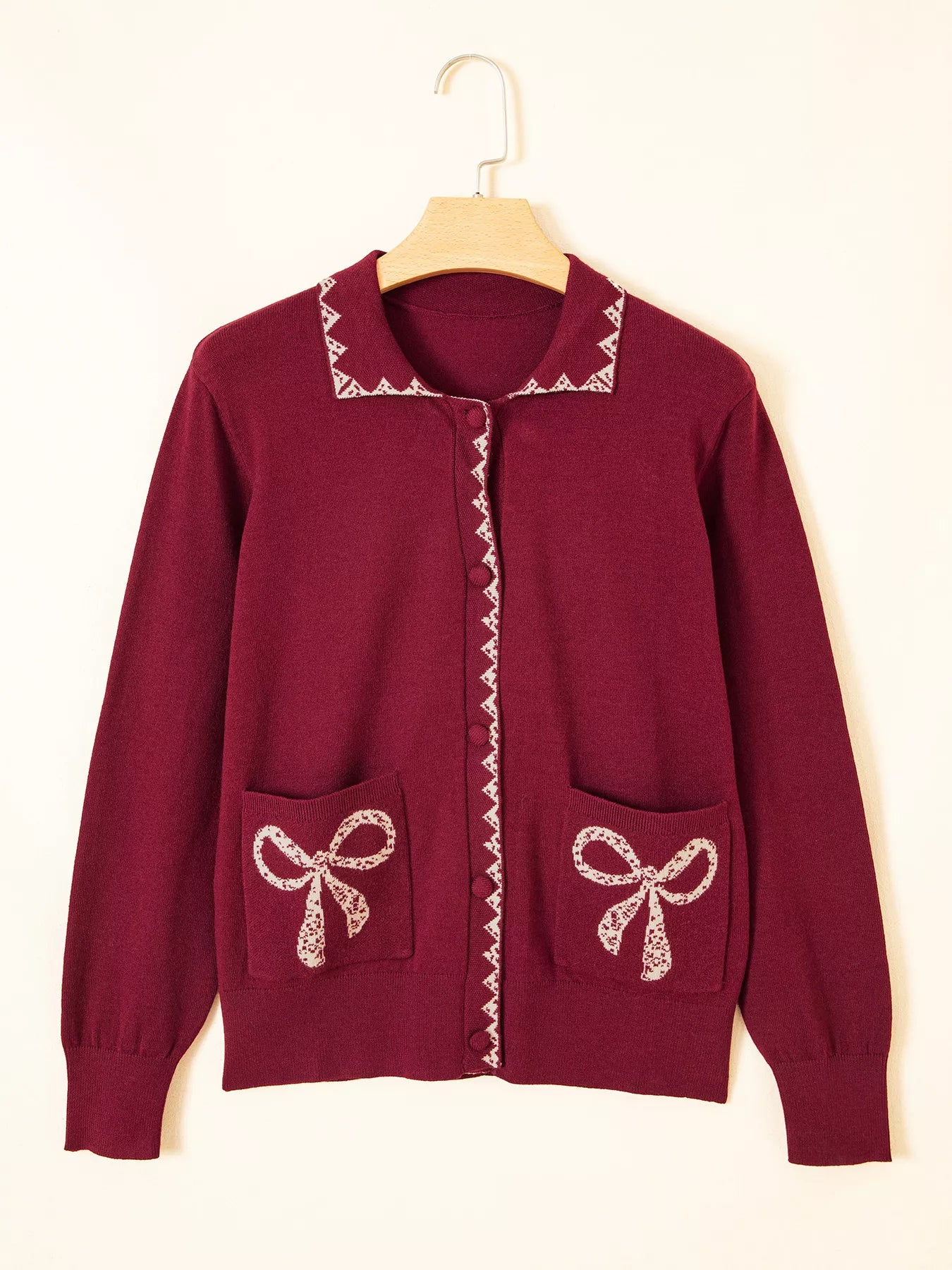 Burgundy knit cardigan with lace trimmed collar and bow pockets on a hanger
